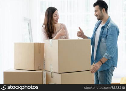 Latino man with beard and Asian woman couple help to carry packed cardboard boxes into their new home and thumbs up to each other after do good job. Mixed race family moving in new house together