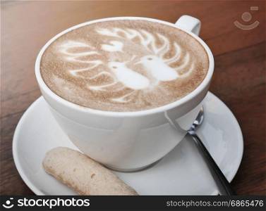 latte art coffee with two birds pattern and cookie in a white cup on wooden background