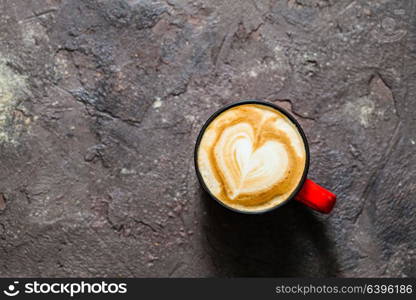 Latte art heart shape in the cup of cappuccino. Top view, vintage red cup on brown concrete textured background. Cup of cappuccino