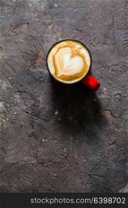Latte art heart shape in the cup of cappuccino. Top view, vintage red cup on brown concrete textured background. Cup of cappuccino