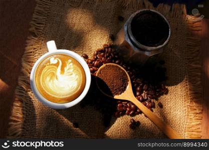 latte cofee , softlight on white art bird on coffee surface with roasted coffee beans ground coffee on wood spoon mocca pot