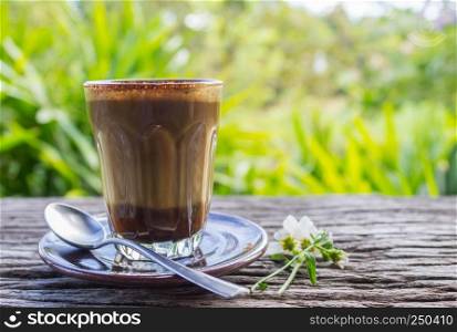 Latte Coffee and Daisy Flower and Spoon on Wood Table with Tree Background Left Eye Level. Relax coffee break time in coffee shop on left frame eye level