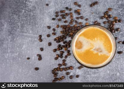 Latte coffee in a glass with cream on gray background with scattering of coffee beans. Top view, flat lay with copy space.. Latte coffee in a glass with coffee cream.