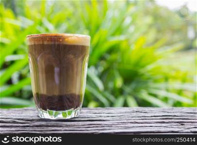 Latte Coffee in Glass on Wood Table with Natural Green Tree Background Eye Level Left. Latte coffee in coffee shop or cafe with nature green tree relax emotion background