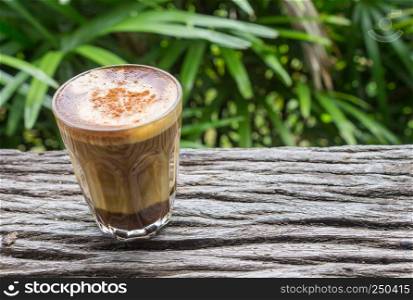 Latte Coffee in Glass on Wood Table with Natural Green Tree Background Left. Latte coffee in coffee shop or cafe with nature green tree relax emotion background