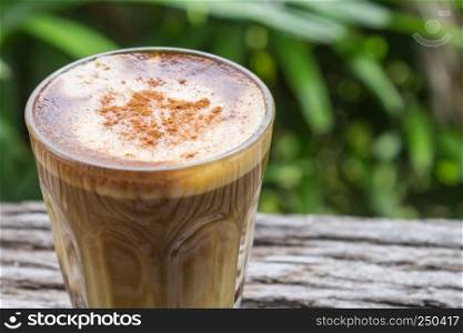 Latte Coffee in Glass on Wood Table with Natural Green Tree Background Zoom. Latte coffee in coffee shop or cafe with nature green tree relax emotion background