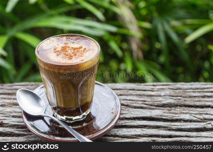 Latte Coffee in Glass with Spoon on Wood Table on Natural Green Tree Background Left Zoom. Latte coffee in coffee shop or cafe with nature green tree relax emotion background