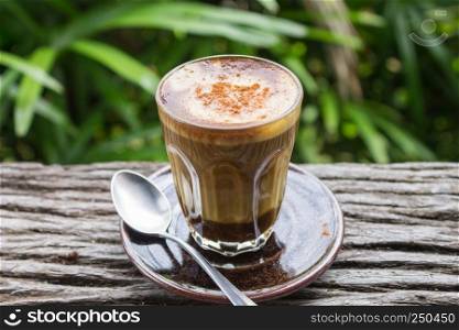 Latte Coffee in Glass with Spoon on Wood Table on Natural Green Tree Background. Latte coffee in coffee shop or cafe with nature green tree relax emotion background