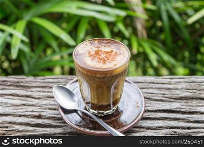 Latte Coffee in Glass with Spoon on Wood Table on Natural Green Tree Background Center. Latte coffee in coffee shop or cafe with nature green tree relax emotion background