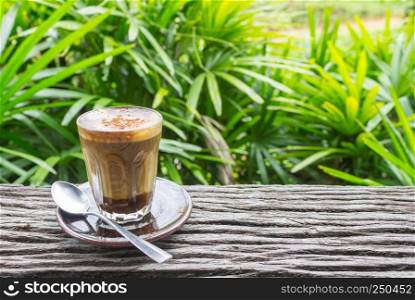 Latte Coffee in Glass with Spoon on Wood Table on Natural Green Tree Background Left. Latte coffee in coffee shop or cafe with nature green tree relax emotion background