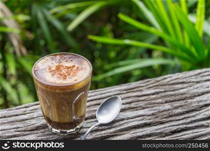 Latte Coffee in Glass with Spoon on Wood Table on Natural Green Tree Background Left. Latte coffee in coffee shop or cafe with nature green tree relax emotion background