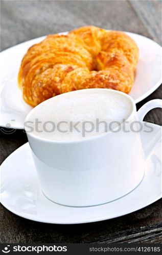Latte coffee with frothed milk and fresh croissant