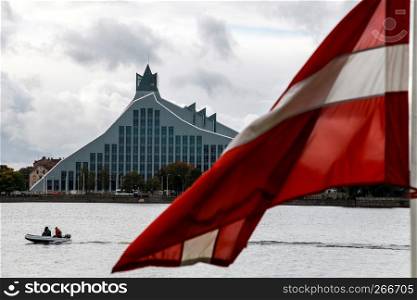 Latvian National Library. Cityscape from November 11 embankment with Latvian National Library, Latvia flag and motor boat in Riga. River Daugava and National Library. National Library in center of Riga.