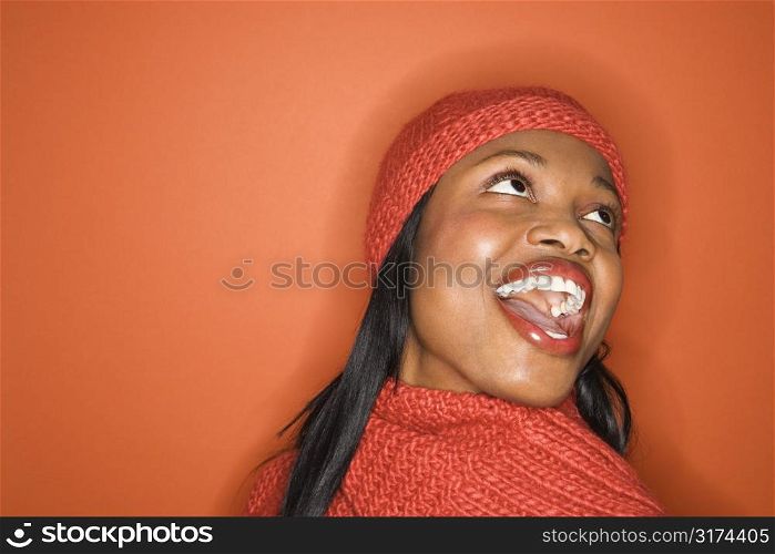 Laughing African-American mid-adult woman wearing orange scarf and hat on orange background.