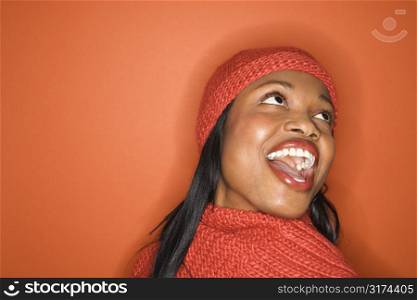 Laughing African-American mid-adult woman wearing orange scarf and hat on orange background.