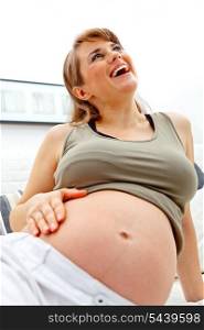 Laughing beautiful pregnant woman relaxing on sofa at home and holding her belly&#xA;
