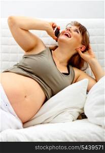 Laughing beautiful pregnant woman relaxing on sofa at home and talking mobile phone.&#xA;