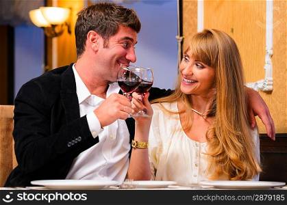 laughing embracing couple is sitting at restaurant and drinking wine
