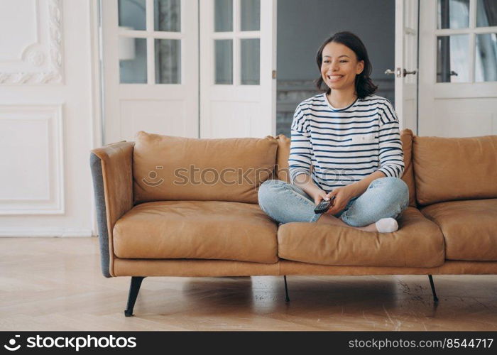 Laughing female watching television, comedy TV show, sitting on comfortable sofa, resting at home. Happy woman having fun enjoying series or movie on couch in living room on weekend.. Laughing female watching television, comedy TV show, sitting on comfortable sofa, resting at home