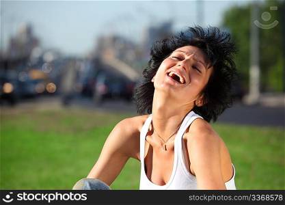 laughing girl sits on lawn at road in city