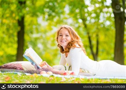 laughing girl with a good book on the grass in the summer park