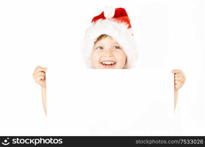 Laughing little boy in a suit of santa shows the blank sheet, isolated