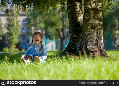 Laughing little girl sitting in grass near the tree