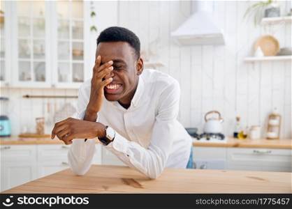 Laughing man sitting at the counter on the kitchen. Cheerful male person poses at the table at home in the morning. Laughing man sitting at the counter on kitchen