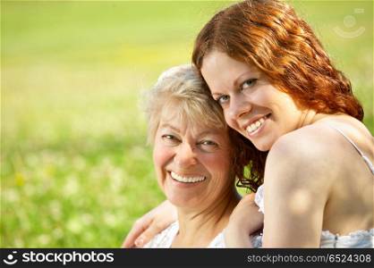 Laughing mother and the daughter sit in embraces on a lawn. Happy family