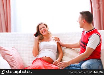 Laughing pregnant woman sitting with husband on couch and speaking phone&#xA;