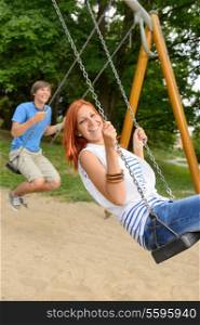 Laughing teenage couple on swing in park have fun together