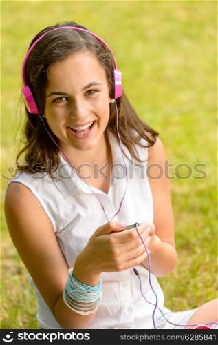 Laughing teenage girl listening to music sitting on grass summer