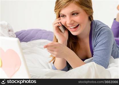 Laughing teenager relaxing by speaking on phone and using laptop