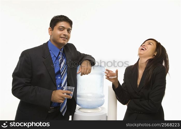 Laughing Vietnamese businesswoman standing at water cooler with Indian businessman.