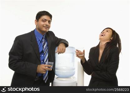 Laughing Vietnamese businesswoman standing at water cooler with Indian businessman.