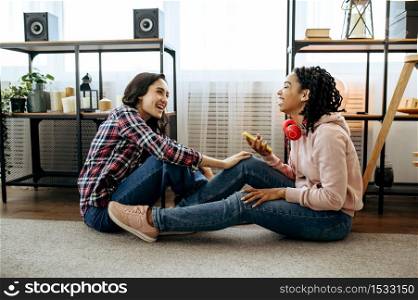 Laughing women in headphones enjoys listening to music at home. Pretty girlfriends in earphones relax in the room, sound lovers resting on couch, female friends leisures together. Laughing women enjoys listening to music at home