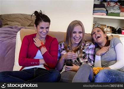Laughing young girls watching TV together sitting on couch
