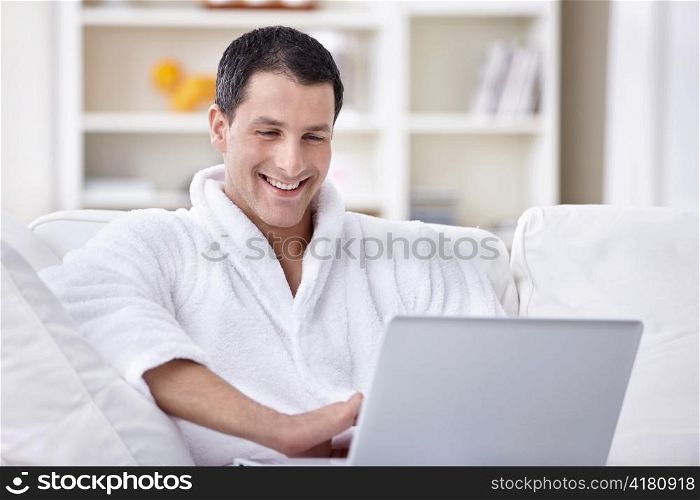 Laughing young man in a bathrobe looking at laptop
