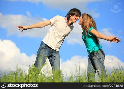 laughing young pair looks against each other in grass against sky
