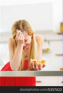 Laughing young woman eating fresh fruits salad in kitchen