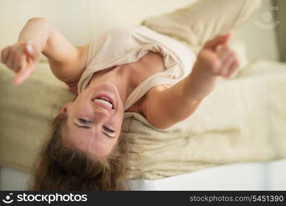 Laughing young woman laying on couch and pointing in camera