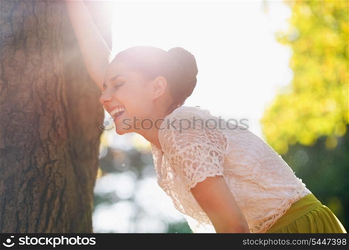 Laughing young woman lean against tree