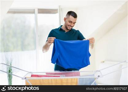 laundry and household concept - happy man taking clothes from drying rack and putting them to basket at home. smiling man with laundry and drying rack at home. smiling man with laundry and drying rack at home