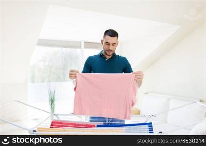 laundry and household concept - happy man taking clothes from drying rack and putting them to basket at home. smiling man with laundry and drying rack at home. smiling man with laundry and drying rack at home