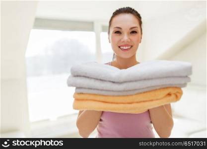 laundry and household concept - happy woman or housewife with pile of bath towels at home. smiling woman with pile of bath towels at home. smiling woman with pile of bath towels at home