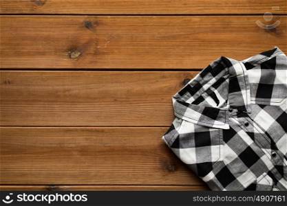 laundry, clothes, fashion and objects concept - close up of checkered shirt on wooden background. close up of checkered shirt on wooden background