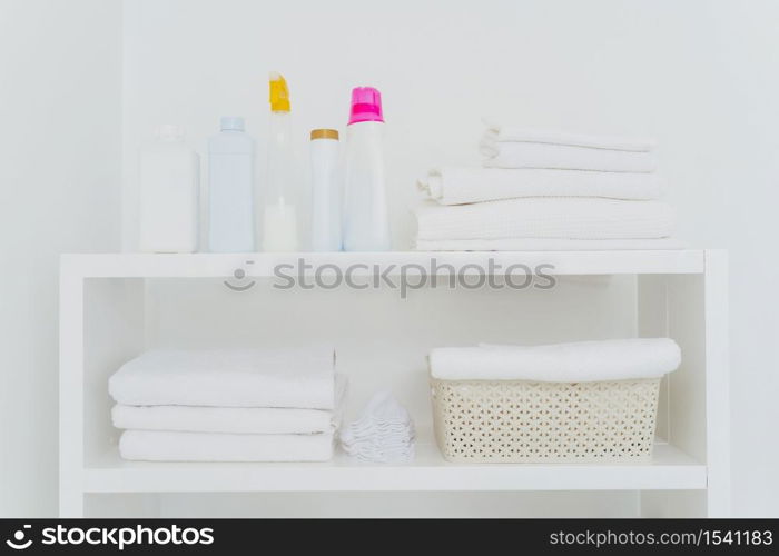 Laundry room with neatly folded towels, bottles of liquid washing or detergents. Everything in white colors. Daily chores and laundry day