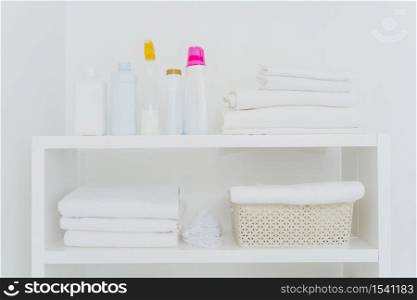 Laundry room with neatly folded towels, bottles of liquid washing or detergents. Everything in white colors. Daily chores and laundry day