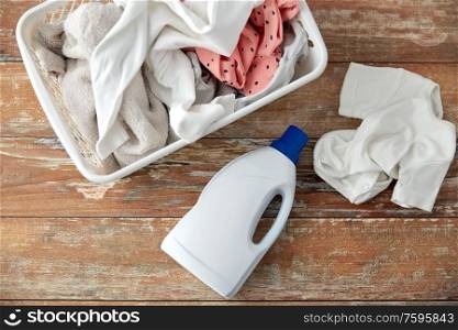laundry, wash and housekeeping concept - baby clothes in basket with detergent or conditioner bottles on wooden table at home. baby clothes in laundry basket with detergent