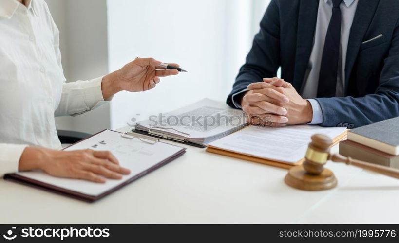 law concept The man in dark blue suit, a lawyer, sitting at his desk and trying to prepare to give law consultation to his customer with his assistance, the man in white shirt.